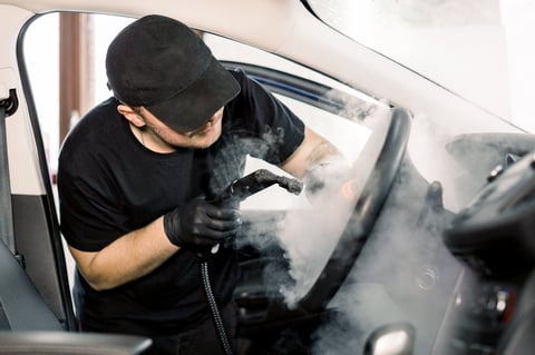 Professional detailer steam cleaning luxury car interior in modern workshop