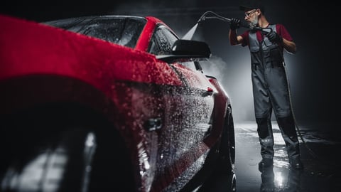 Professional car wash specialist using high pressure washer on red sports coupe