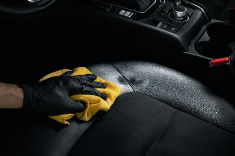 Car interior cleaning and detailing - man cleaning black alcantara leather seat with foam