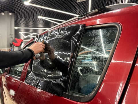 Applying tinting foil on car window in tuning studio