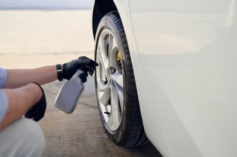 Car detailer meticulously cleaning luxury car wheel and tire with spray bottle in workshop