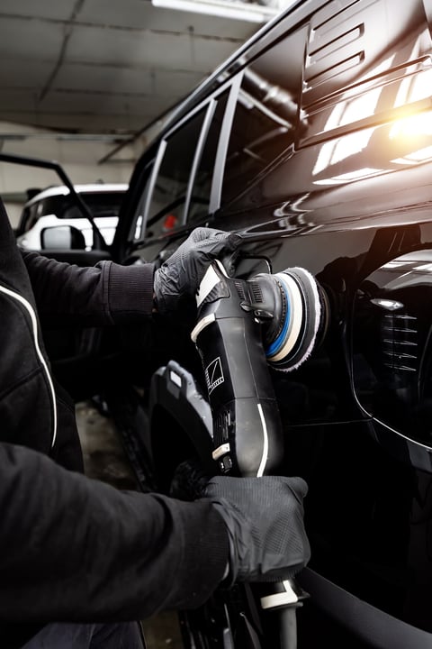 Professional detailer using orbital polisher on luxury car in modern indoor detailing center