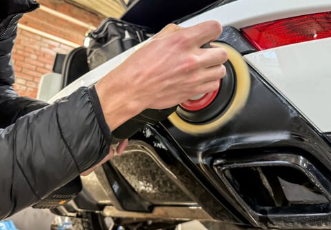 Car worker polishing car body with orbital polishing machine
